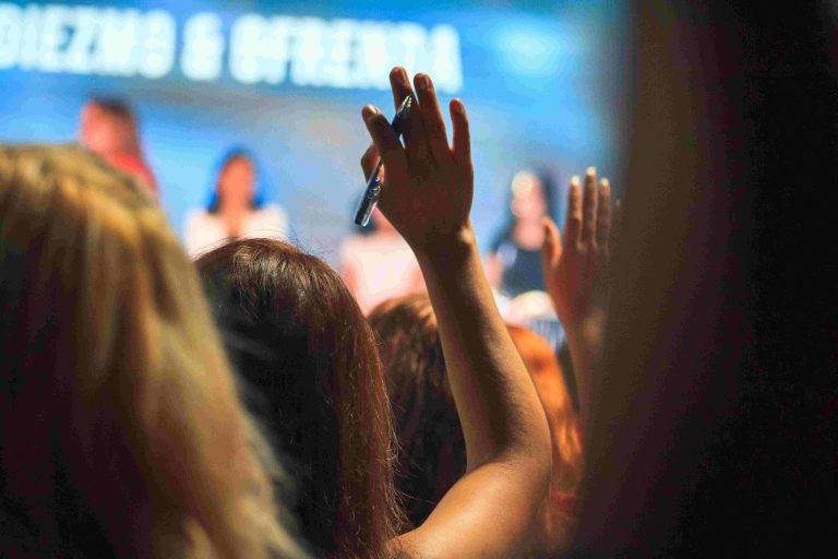 An image of a woman raising her hand in the audience of a conference.