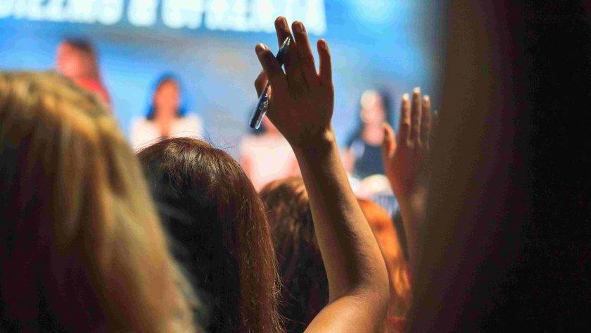 An image of a woman raising her hand in the audience of a conference.