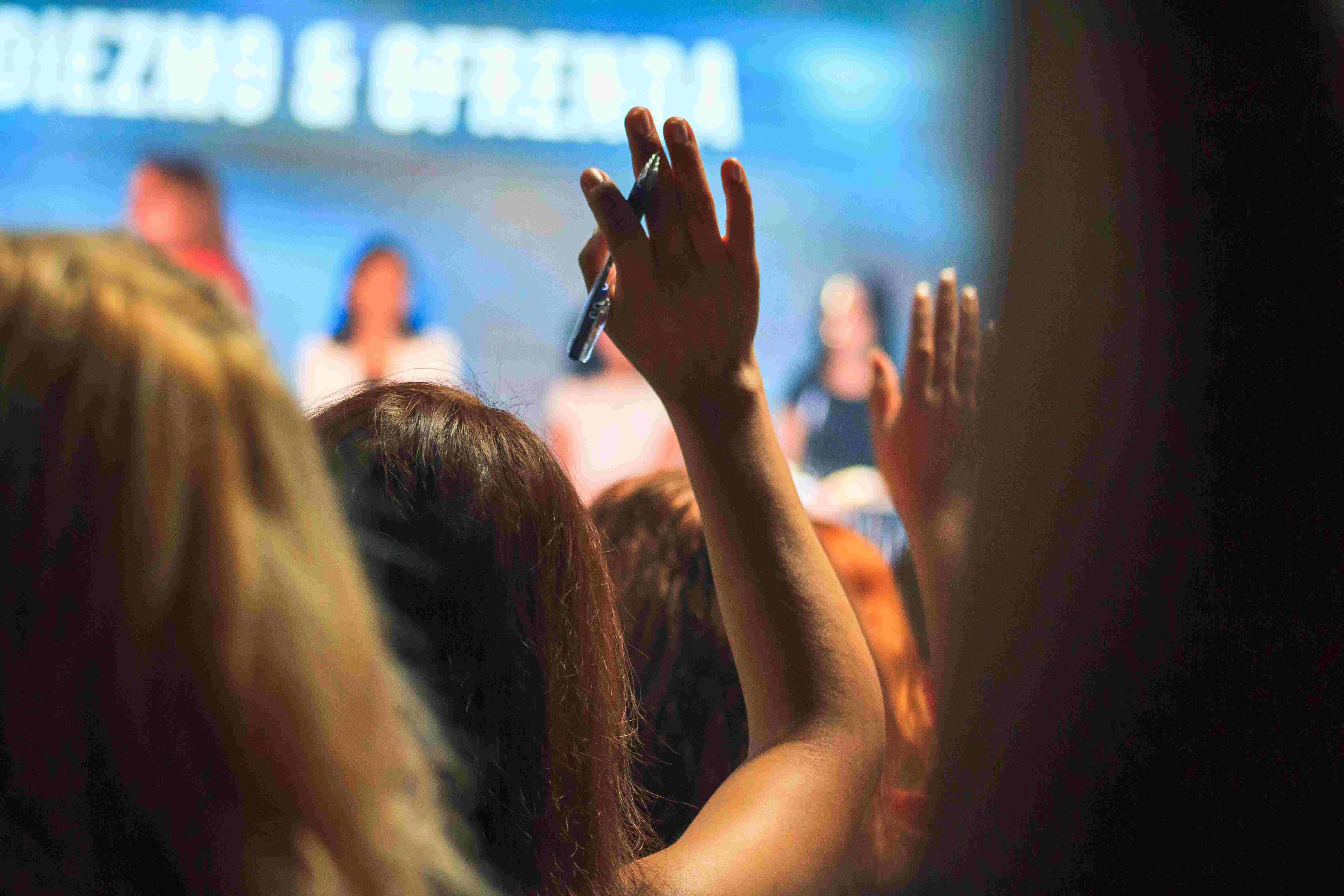 An image of a woman raising her hand in the audience of a conference.